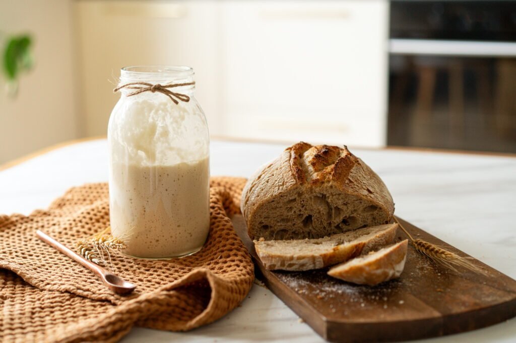 Freshly baked sourdough bread with a jar of starter and rustic cloth