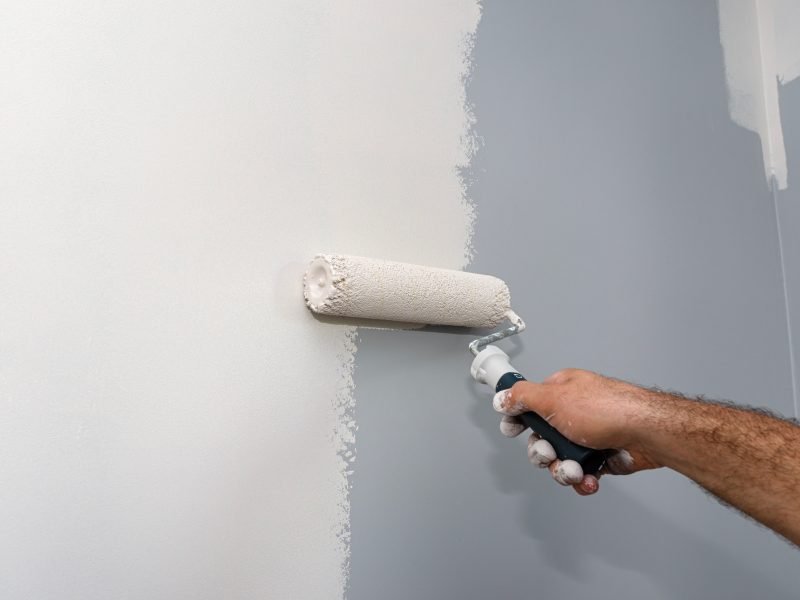 Painter paints a room in beige color using a paint roller at home.